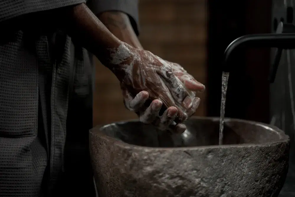 Hands lathered with soap being washed under running water over a stone basin